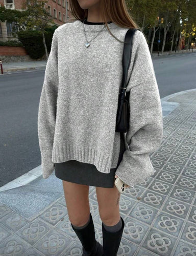 Person wearing a gray sweater and black skirt on a street.