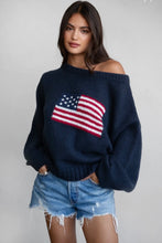 Load image into Gallery viewer, A woman wearing a navy blue off-the-shoulder knit sweater with a large American flag motif on the front, paired with distressed denim shorts, against a plain light gray background.
