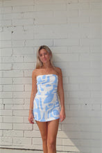 Load image into Gallery viewer, Woman wearing a strapless dress with blue abstract pattern against a white brick wall.
