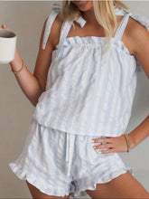 Load image into Gallery viewer, A woman wearing a light blue and white vertically striped two-piece romper with tie straps and ruffled edges, holding a white mug against a neutral beige background.
