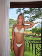 Load image into Gallery viewer, Woman in a white bikini standing on a balcony with a garden view.
