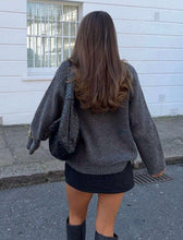 Load image into Gallery viewer, Person wearing a gray sweater and black skirt with a black bag, standing on a street.
