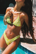 Load image into Gallery viewer, A woman wearing a yellow and green floral triangle bikini leans against the edge of a swimming pool, with her head tilted back in bright outdoor sunlight.
