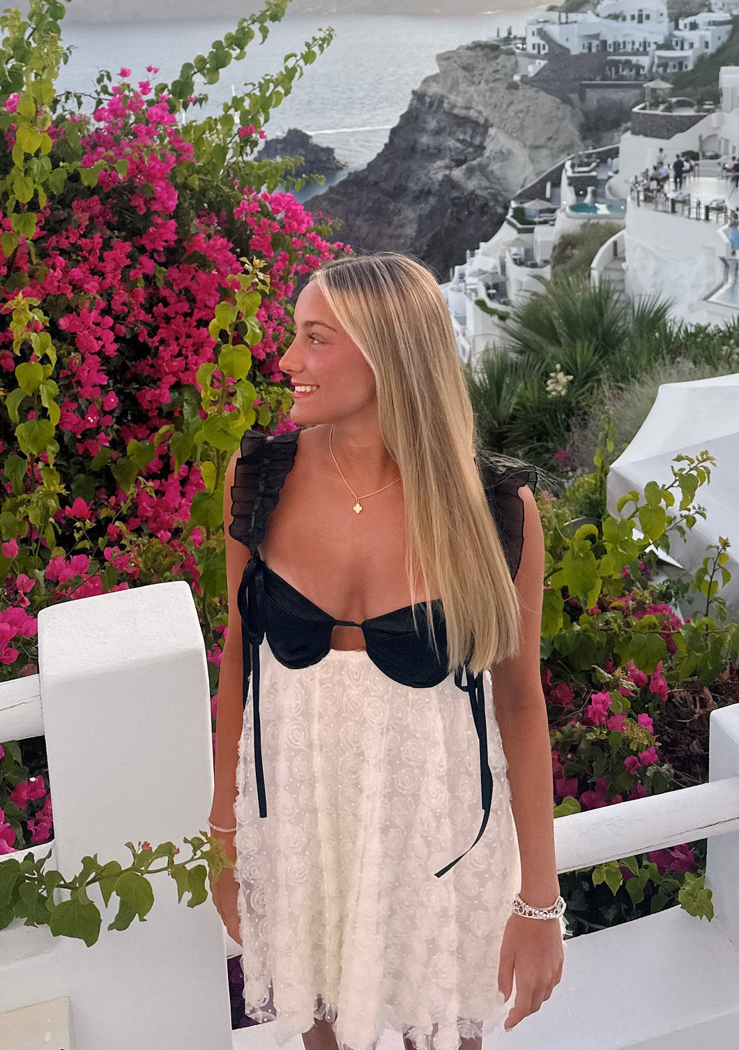 Woman in a black and white outfit standing in front of pink flowers and a scenic background.