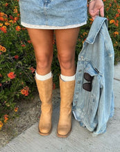 Load image into Gallery viewer, A person outdoors wearing light blue denim shorts and tan suede knee-high boots, holding a light blue denim jacket with sunglasses in the pocket. Orange flowers and green foliage are in the background.

