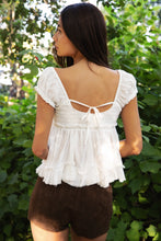 Load image into Gallery viewer, Woman wearing a white ruffled top and brown shorts in a green outdoor setting
