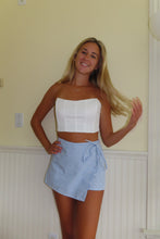 Load image into Gallery viewer, Woman wearing a white top and blue striped skirt standing against a plain wall.
