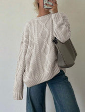 Load image into Gallery viewer, Person wearing a beige cable knit sweater and blue jeans, holding a phone with a patterned case.
