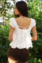 Load image into Gallery viewer, Woman wearing a white ruffled top and brown shorts in a green outdoor setting
