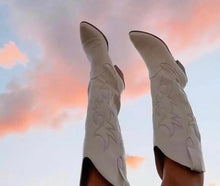 Load image into Gallery viewer, A pair of knee-high cowgirl boots against a sky with clouds during either sunrise or sunset.
