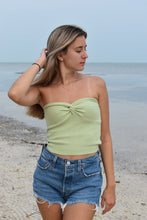 Load image into Gallery viewer, A woman wearing a light green twisted knit top and blue denim shorts, standing by the beach.

