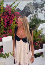 Load image into Gallery viewer, Woman in a black and white outfit standing in front of pink flowers and a scenic background.
