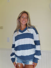 Load image into Gallery viewer, A woman wearing an oversized blue and white striped V-neck sweater, smiling and posing with one hand on her hip.
