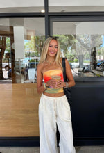 Load image into Gallery viewer, A person wearing a multicolored tube top in shades of orange, green, and red, paired with white pants.
