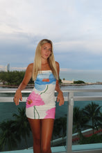 Load image into Gallery viewer, Woman in a colorful dress standing by a pool with palm trees in the background
