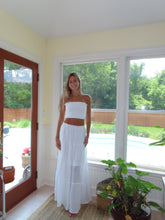 Load image into Gallery viewer, Woman in a white dress standing in front of a large window with a view of greenery.
