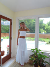 Load image into Gallery viewer, Woman in a white dress standing in front of a large window with a view of greenery.
