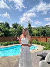 Load image into Gallery viewer, Woman in a white dress standing by a pool with a blue sky and trees in the background
