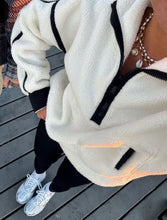 Load image into Gallery viewer, Close-up of a person wearing a white fleece jacket with black zippers on a wooden deck.

